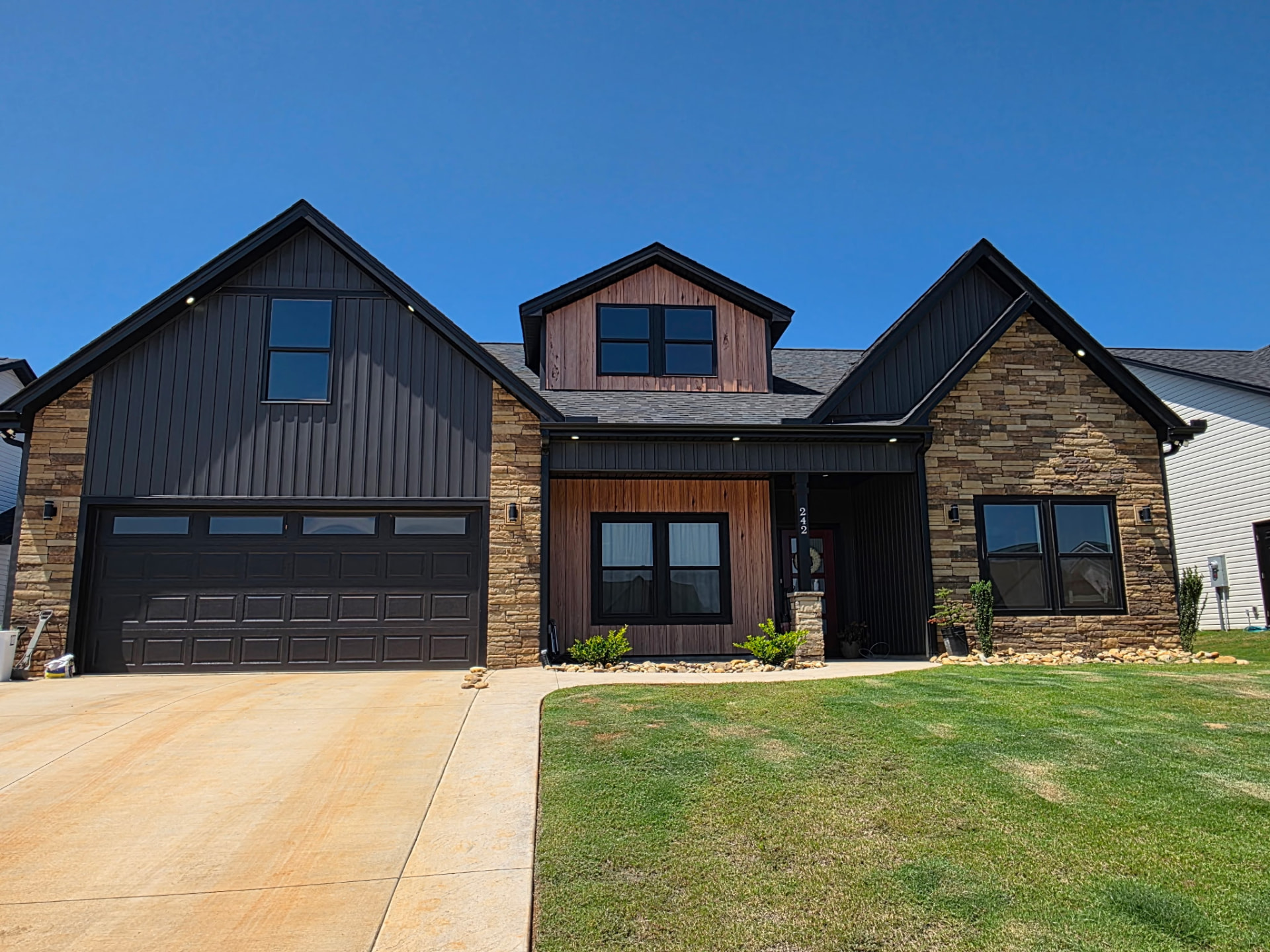 Home with brown and tan ledge stone, dark siding, and cedar entry detail