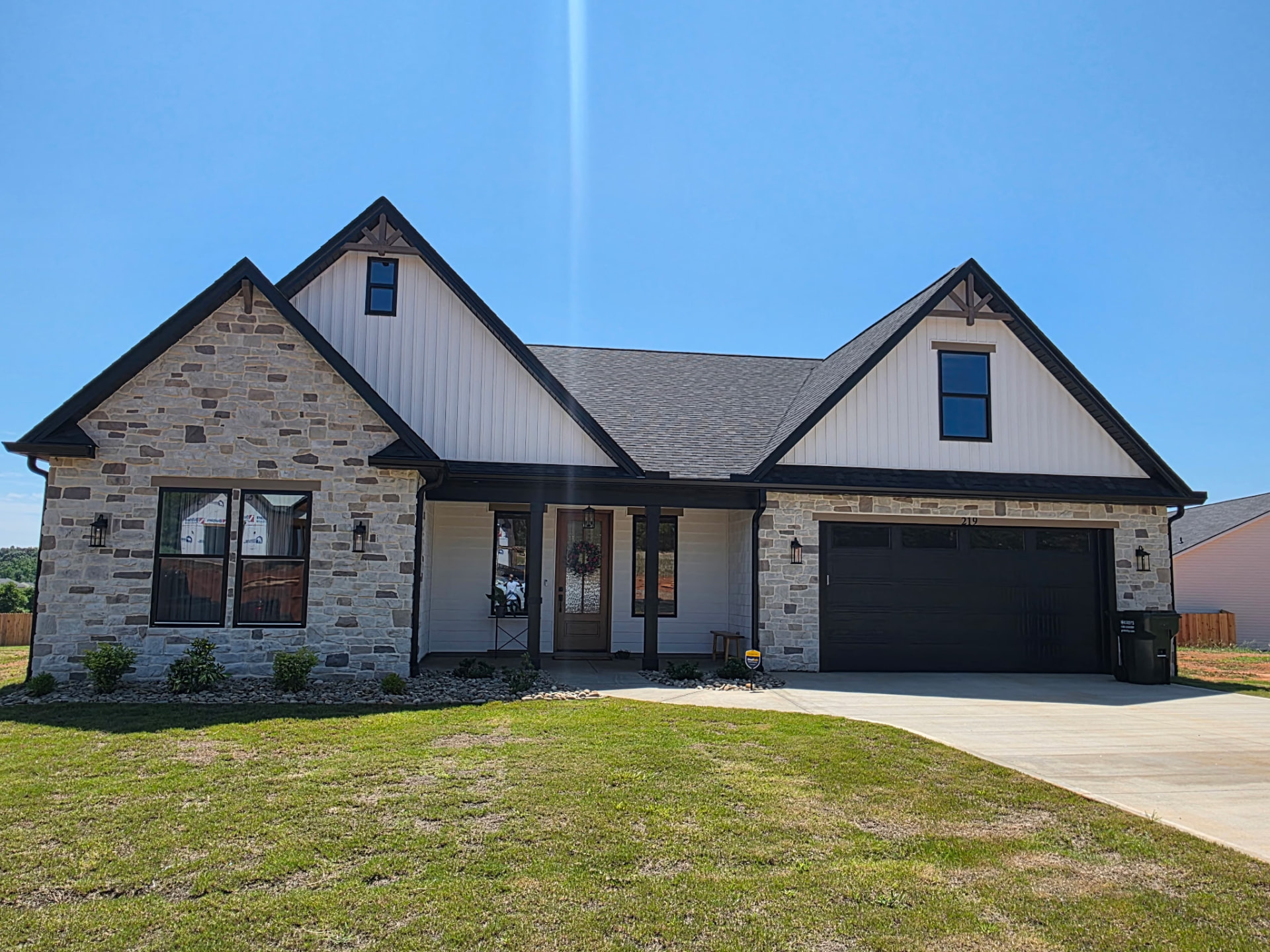 Completed residential stone veneer home with white siding and black trim