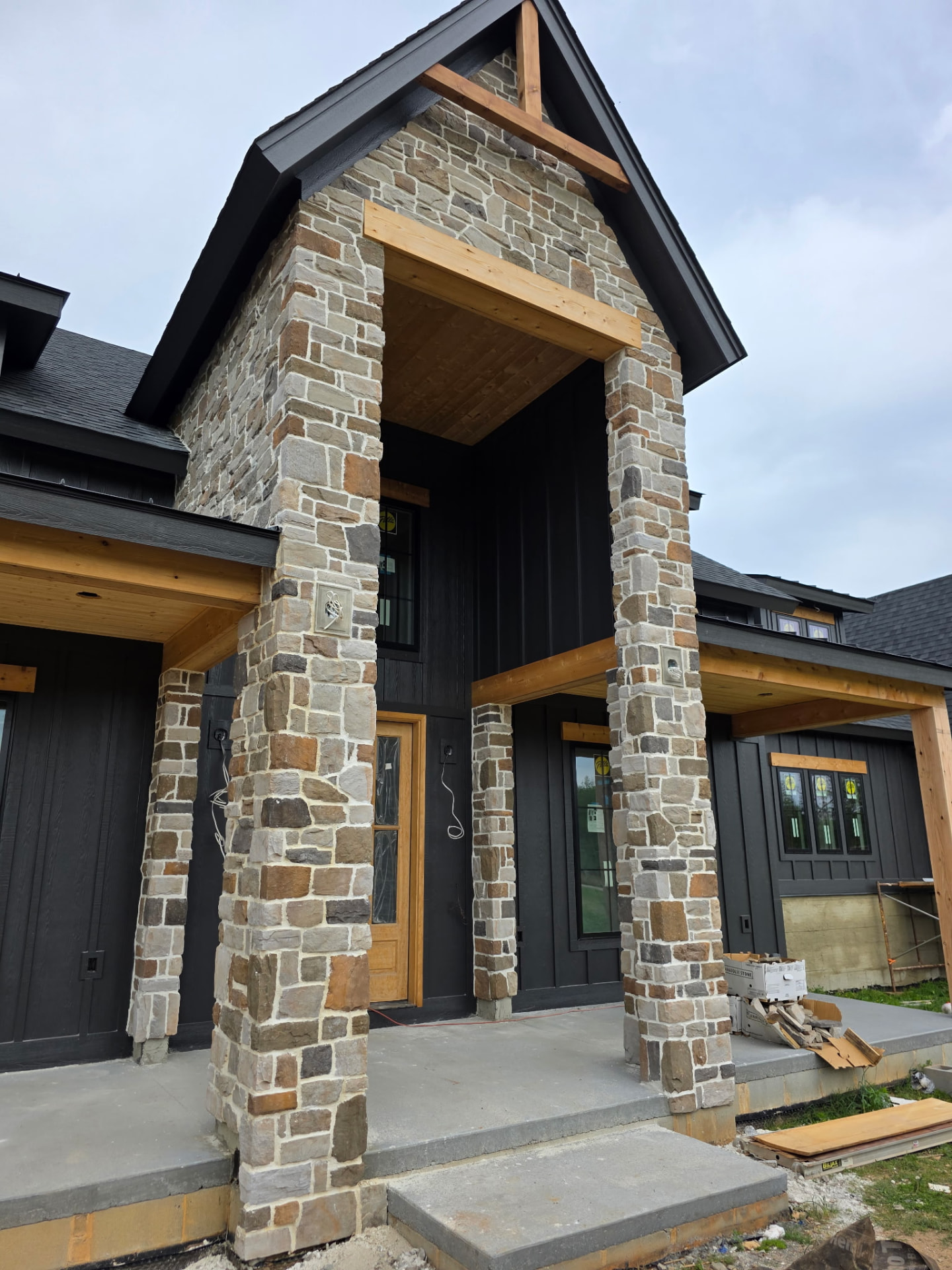 Custom residential stone entrance with tall stone columns, stone-covered gable, and natural wood accents by Premier Landscape Rock
