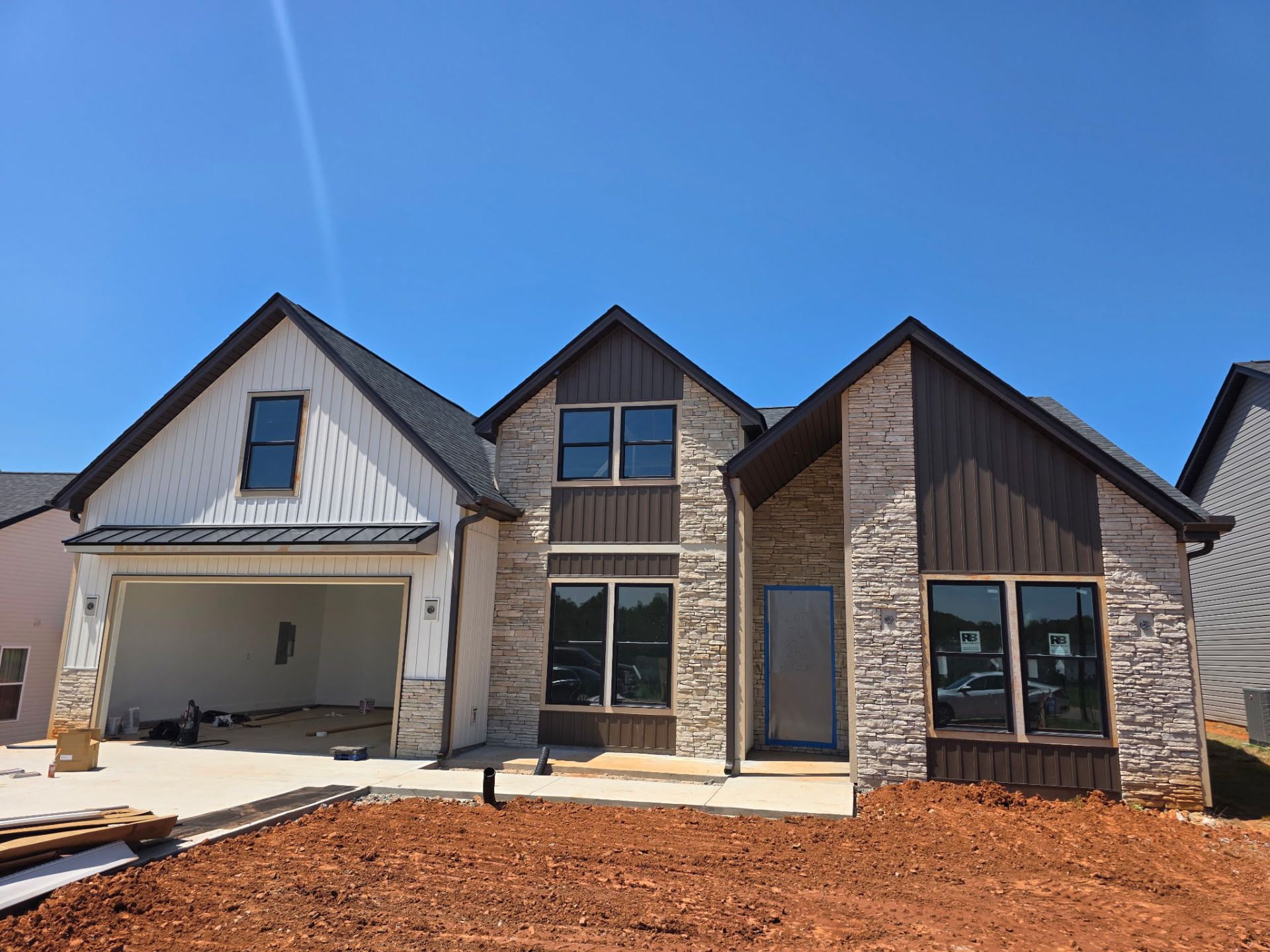 New construction home with mixed ledge stone gables and dark board-and-batten siding