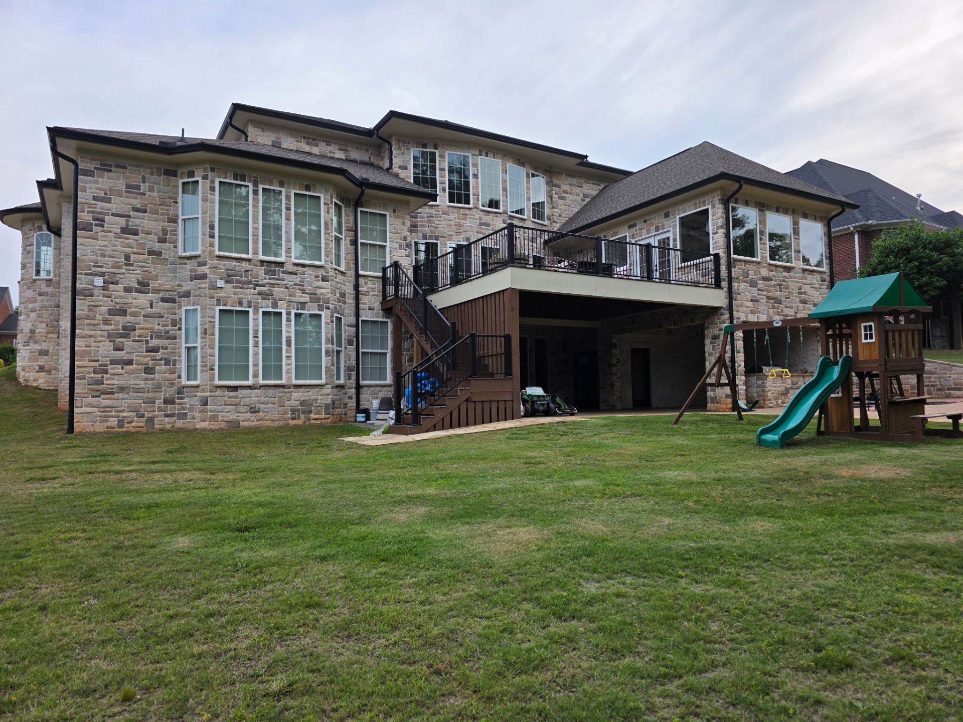 Two-story rear elevation clad in tan and gray natural stone with a covered lower level